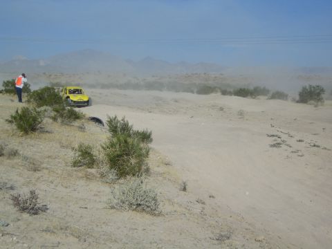 Yellow race buggy stopped on a desert trail with a flagger in orange vest nearby
