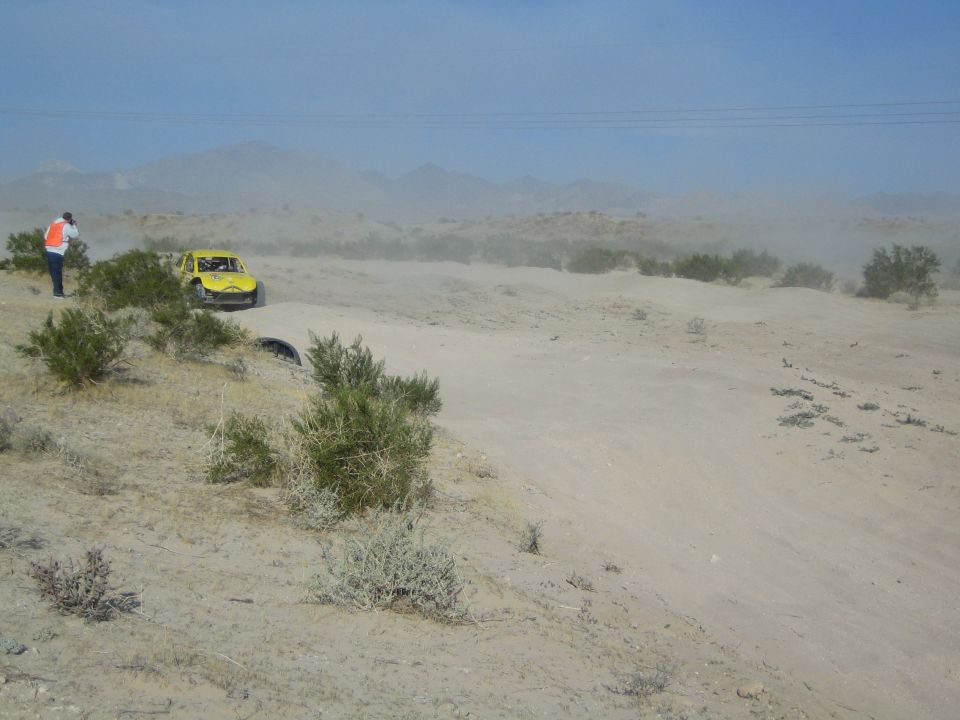 Yellow race buggy stopped on a desert trail with a flagger in orange vest nearby
