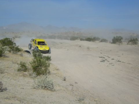 Yellow off-road race buggy airborne over a desert rise