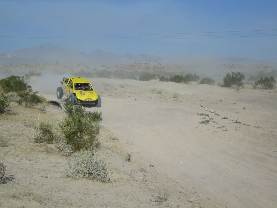 Yellow off-road race buggy airborne over a desert rise