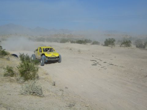 Yellow off-road race buggy speeding across a dusty desert course