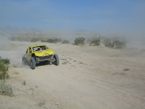 Yellow off-road buggy with helmeted driver racing through desert dust