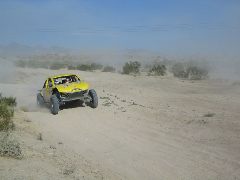 Yellow off-road buggy with helmeted driver racing through desert dust
