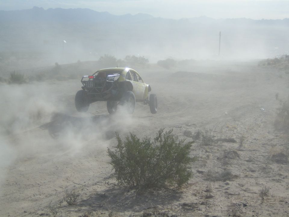 Yellow-green off-road buggy emerging from heavy dust on a desert course
