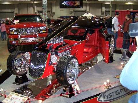 1995 Ford Probe - A custom hot rod with a powerful V8 engine and striking red and black paint is displayed at a show, with a red pickup truck in the backgrou…