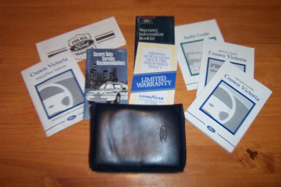 Ford Crown Victoria owner's manual, warranty booklet, audio guide, and police/fleet vehicle documents laid out on a wooden surface