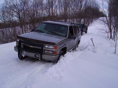 2000 Chevrolet Tahoe - Silver Chevrolet Tahoe and a black pickup truck on a snow-covered road in a wooded area.