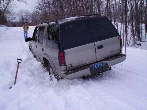 2000 Chevrolet Tahoe - A silver Chevrolet Tahoe is stuck in deep snow on a wooded path, with a person standing nearby.