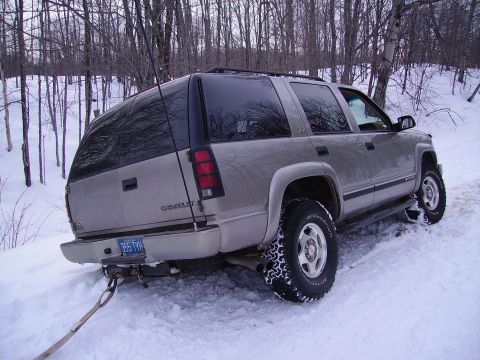 2000 Chevrolet Tahoe - A silver Chevrolet Suburban is stuck in the snow, with a tow strap attached to its rear bumper.