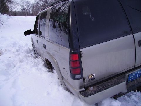 2000 Chevrolet Tahoe - Silver SUV with Z71 badging is stuck in deep snow, with trees and a snowy path visible in the background.