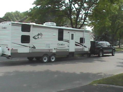 2002 Ford Excursion - Pickup truck tows a travel trailer on a paved road with trees and houses in the background.