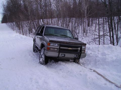 2000 Chevrolet Tahoe - This SUV is stuck in a snowy area, with trees in the background and a tow strap attached to the front.