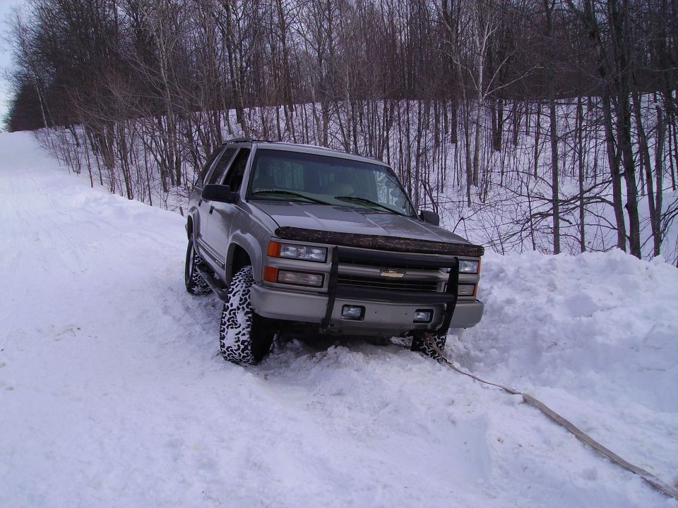 Silver SUV stuck in deep snow on a wooded hill, front bumper has a brush guard