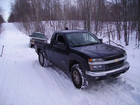2000 Chevrolet Tahoe - A black Chevrolet Colorado pickup truck navigates a snowy road, with another vehicle visible behind it. The 'SUPERMOTORS' watermark is pres…