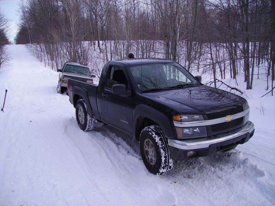 Black Chevrolet Colorado pickup truck in snow, 3/4 front view. Text 'SUPERMOTORS' visible