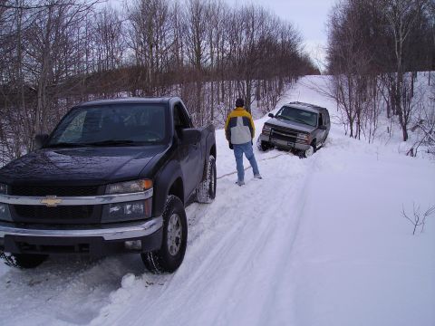 2000 Chevrolet Tahoe - Two vehicles are stuck in the snow on a wooded road, with one SUV partially submerged.