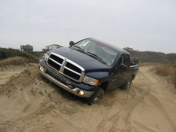 Dark blue Dodge Ram crew cab pickup stuck nose-down in deep beach sand, grille packed with sand