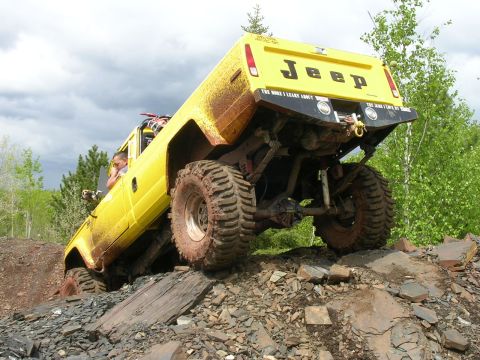 1986 Jeep J-10 - This modified Jeep Comanche is shown tackling a challenging off-road course with steep inclines and rocky obstacles.
