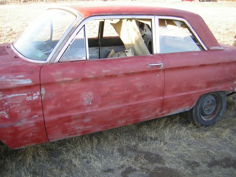 1963 Ford Falcon - Side view of a 1963 Ford Falcon sedan with faded red paint and visible primer.