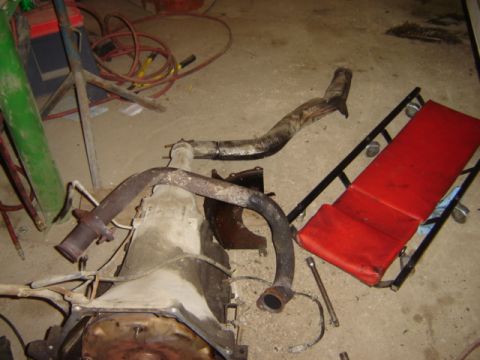 1992 Ford Bronco - Various transmission and exhaust components are laid out on a garage floor, with a red creeper nearby.