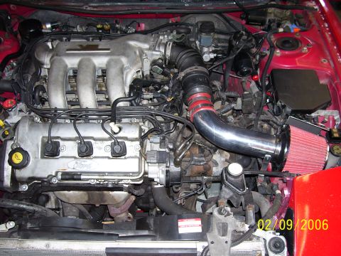 1994 Ford Probe - The engine bay of a red 1994 Ford Probe shows a V6 engine with an aftermarket cold air intake system.