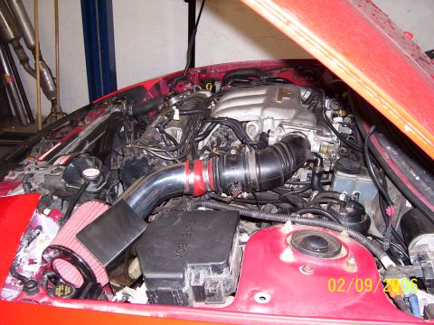 1994 Ford Probe - The engine bay of a red car features an aftermarket air intake system and a visible fuse box, with a date stamp of 02/09/2006.