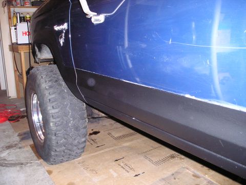 1986 Ford Bronco II - Close-up of a vehicle's side panel and tire, showing body damage and a large off-road tire.