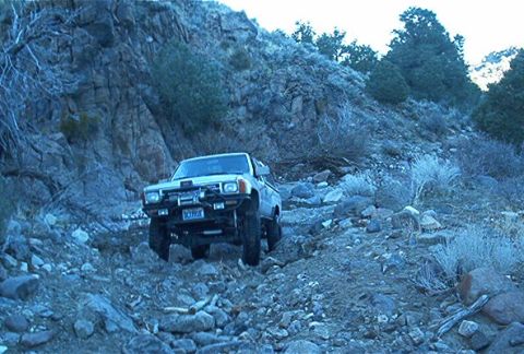 1986 Ford Bronco - Toyota pickup truck tackling a challenging rocky path in a mountainous area.
