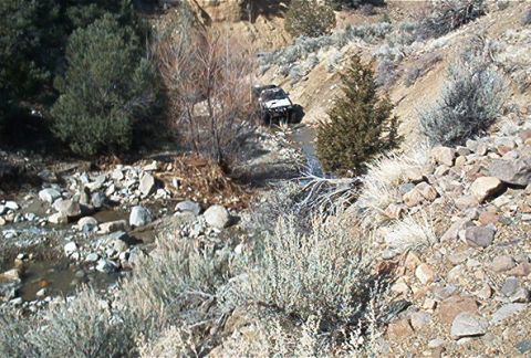 1986 Ford Bronco - A white SUV navigates a dry creek bed in a , natural landscape.