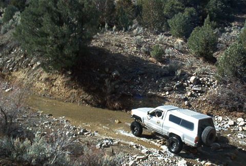 1986 Ford Bronco - This SUV, likely from the 1990s, navigates a rocky, wet terrain.