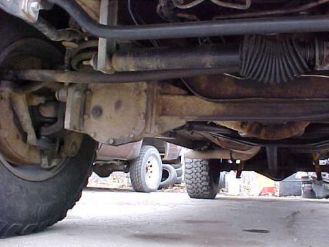 2000 Ford E350 - A low-angle shot reveals the complex undercarriage of a van, with various mechanical parts and another vehicle in the distance.