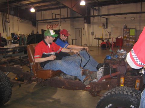 1978 Ford Bronco - Two men sit in the driver's seat of a vehicle chassis in a workshop.