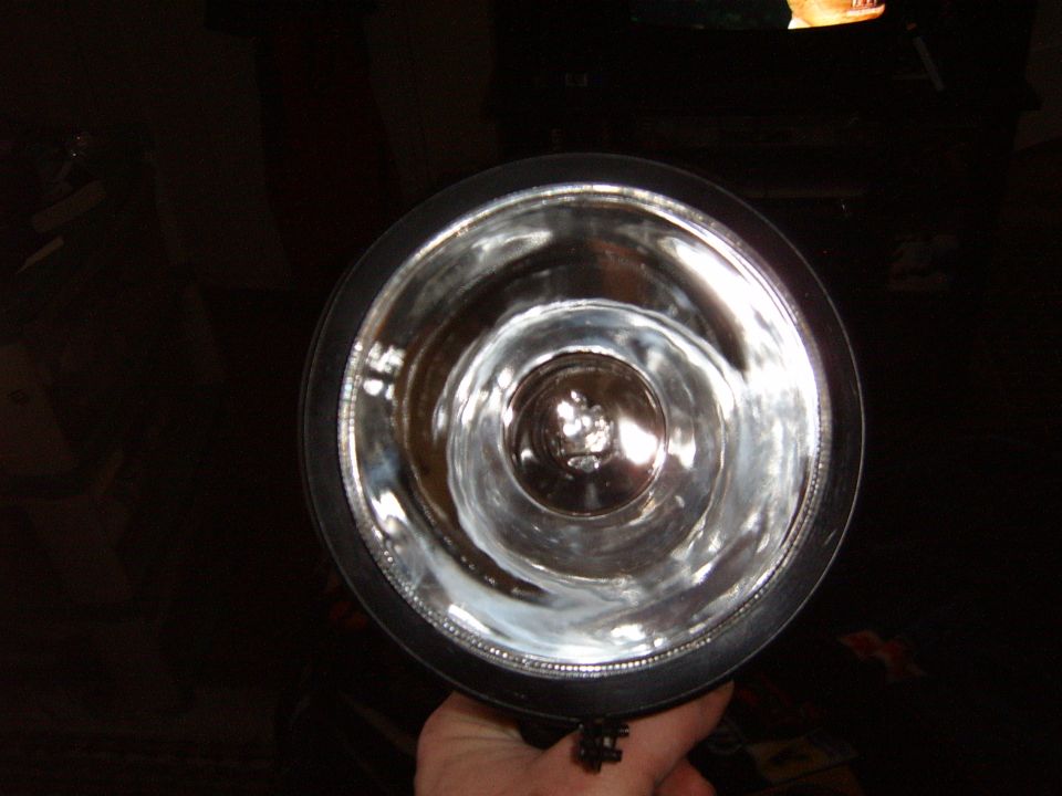 Close-up of a shiny headlight reflector with a black outer rim, held by a hand