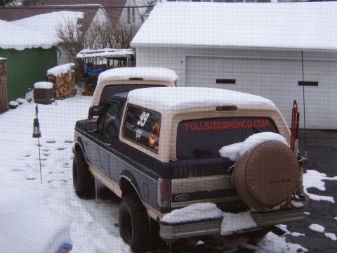 1993 Ford Bronco - Two Ford Broncos are parked outside in the snow, one with a spare tire cover and a website sticker on the rear window.