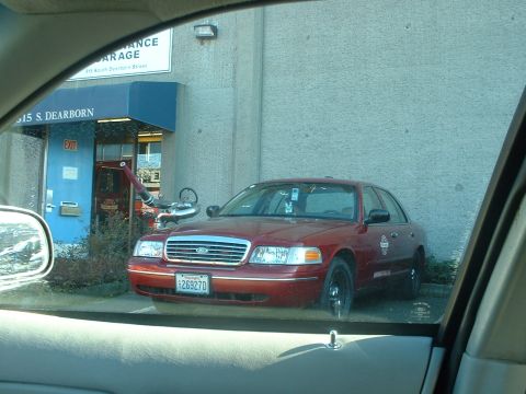 1999 Ford Crown Victoria - A red sedan is parked in front of a building with an awning and signs indicating its address and function.