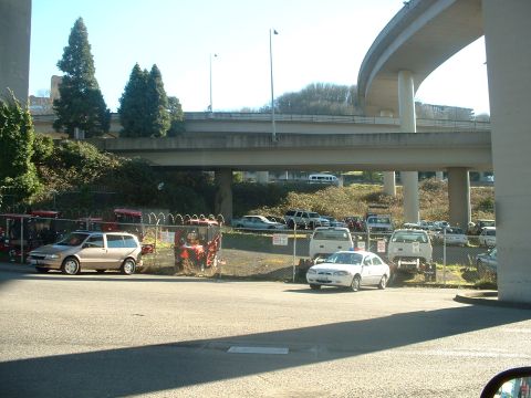 1999 Ford Crown Victoria - A variety of vehicles are parked in a lot beneath a concrete overpass on a sunny day.