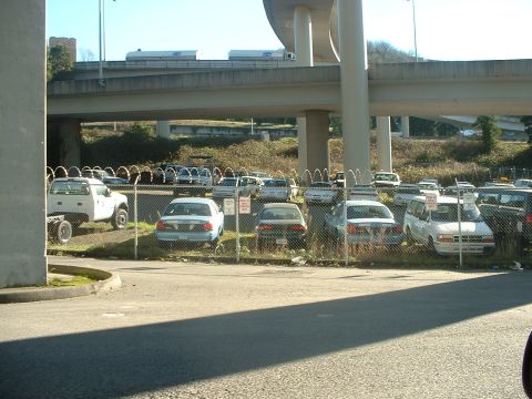 1999 Ford Crown Victoria - A variety of vehicles are parked in an outdoor lot beneath a large concrete overpass.
