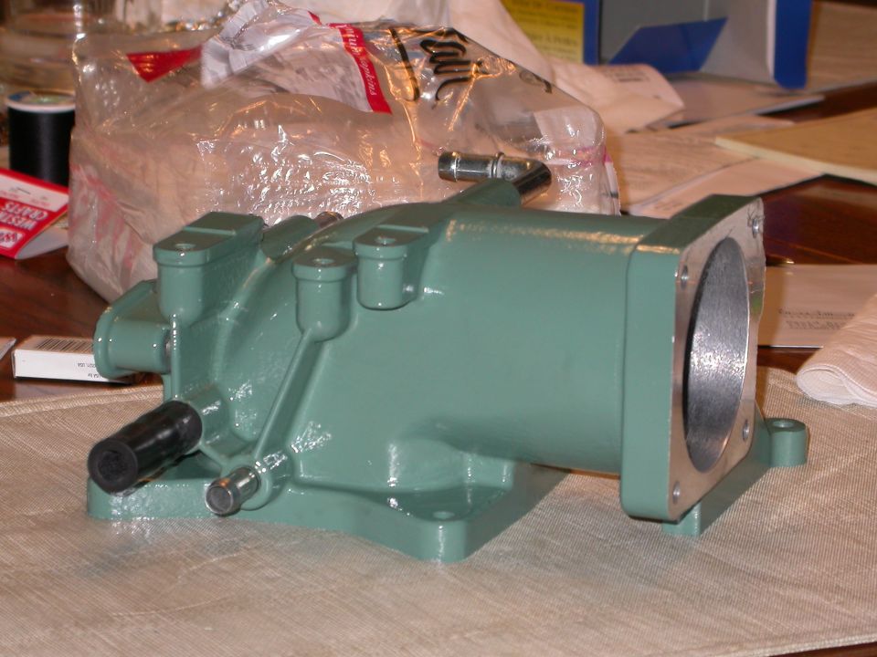 Freshly painted green intake elbow casting with round throttle opening, on a placemat indoors
