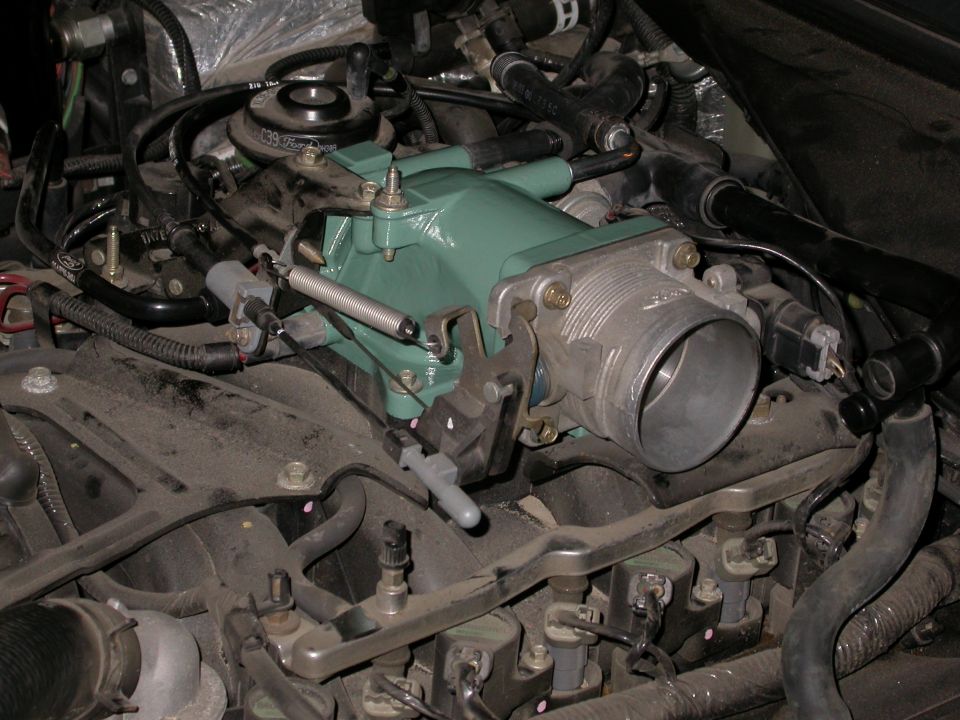 Engine bay closeup: green-painted intake plenum with throttle body and linkage on a Ford V8.