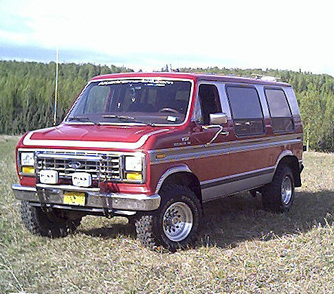 Lifted red Ford Econoline 4x4 van with brush guard in a grassy field