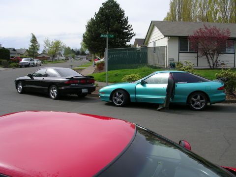 1996 Ford Probe - Two Ford Probes, a teal one with its door ajar and a black one, are parked on a suburban street.
