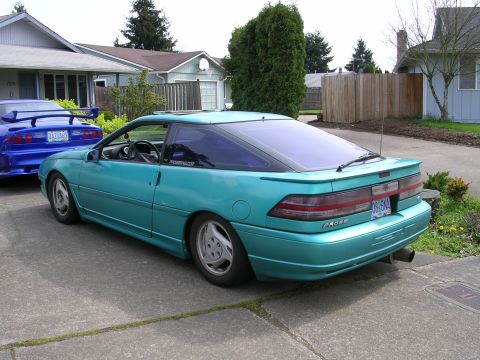 1996 Ford Probe - A teal Ford Probe is parked in a driveway, with another car visible to its left. The rear of the Probe is facing the camera.