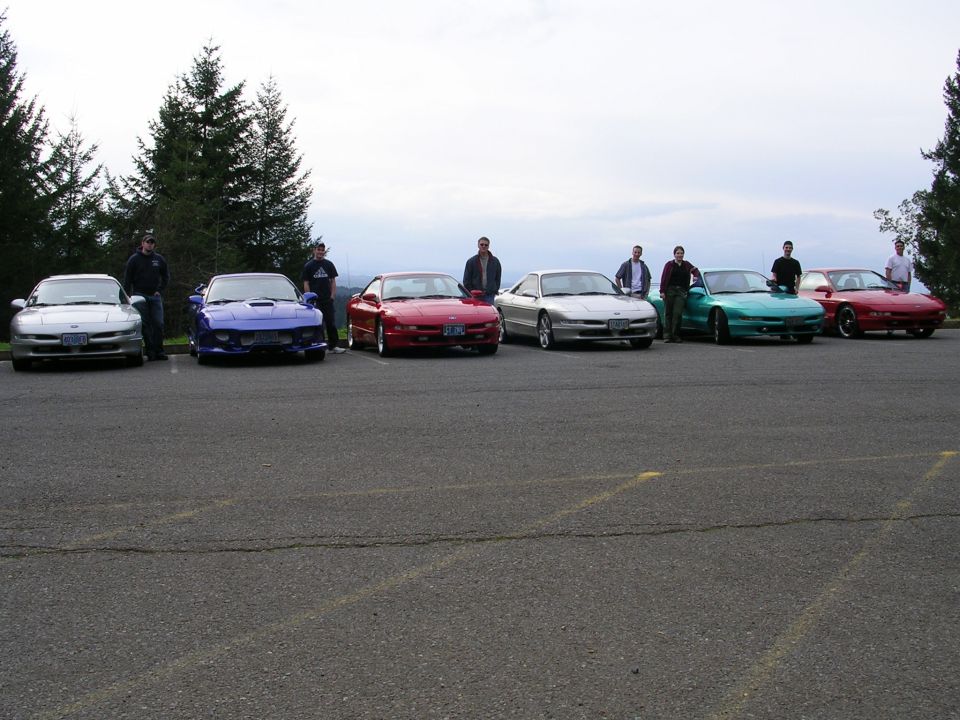 Row of seven Ford Probe coupes in mixed colors at a hilltop parking lot car meet