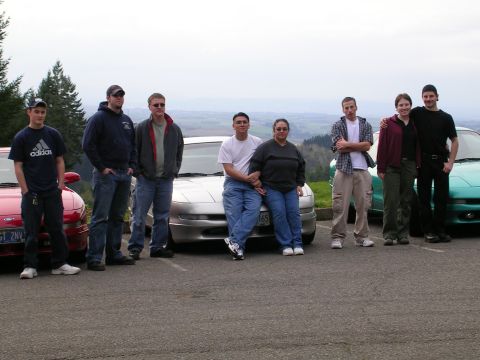 1996 Ford Probe - A group of people gathered around three cars, including a 1996 Ford Probe, outdoors with a scenic view.