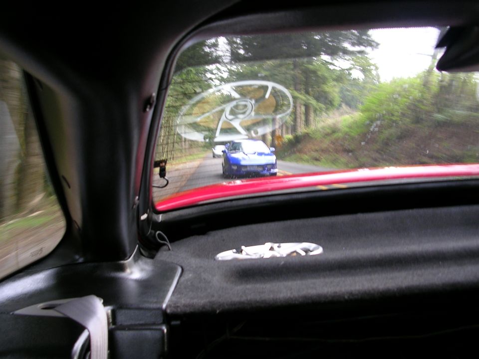 Blue sports car driving on a tree-lined road, seen from inside another vehicle