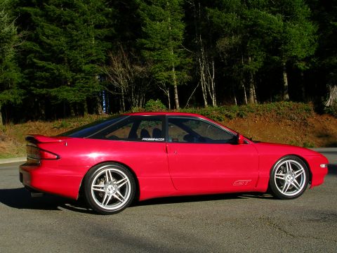1996 Ford Probe - A red coupe with a spoiler and GT badging is parked on a road with trees in the background.