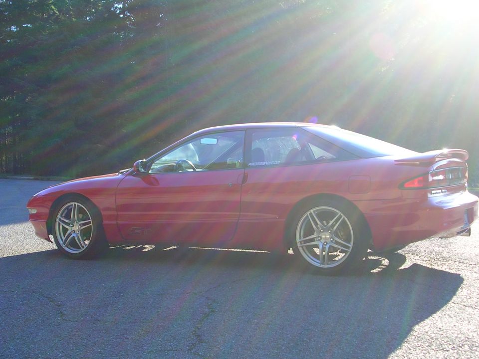 Red coupe parked on asphalt, side view, sun glare
