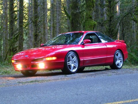 1996 Ford Probe - A red 1996 Ford Probe GT is parked on the side of a road, surrounded by trees, with its headlights illuminated.