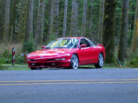 1996 Ford Probe - A red 1996 Ford Probe sits parked beside a forest road.
