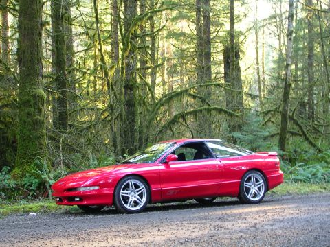 1996 Ford Probe - A red 1996 Ford Probe is parked on a dirt road surrounded by a dense, moss-covered forest.